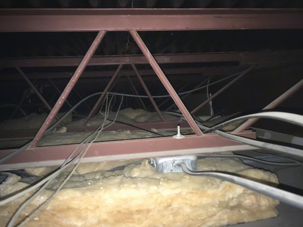 Fiberglass batts laying on top of ceiling panels with wires, outlets and red beams all around it