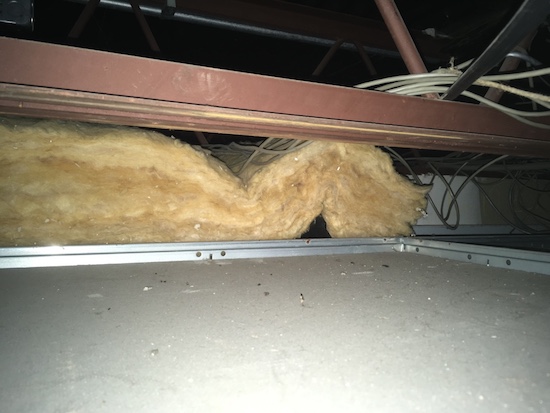 A yellow fiberglass batt laying above a ceiling panel with white wires hanging down and laying on top of the batt.