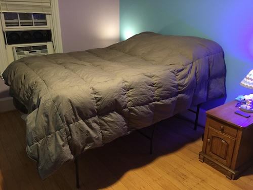 A bed with a gray comforter inside a bedroom with blue walls