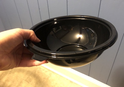 A black single use bowl being held by a person in a kitchen with blue walls
