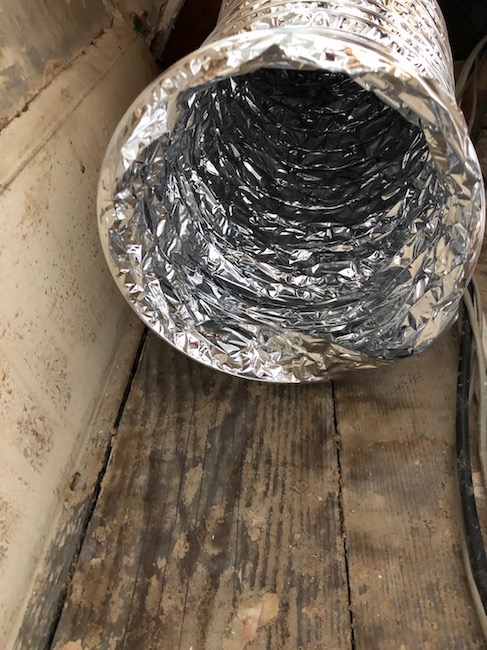 A shiny foil duct inside the bay of a wooden floor