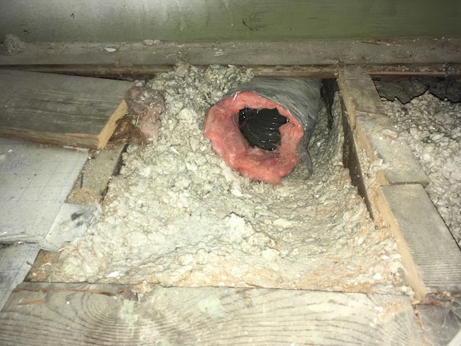 A large black flex duct with pink fiberglass exposed poking out  from the gray blown-in insulation where the floor boards were removed in an attic.