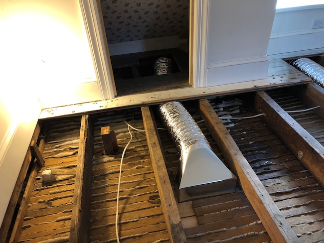 An attic floor with the top layer of wood removed showing the floor joists with clean foil ducts and wires running under the floor