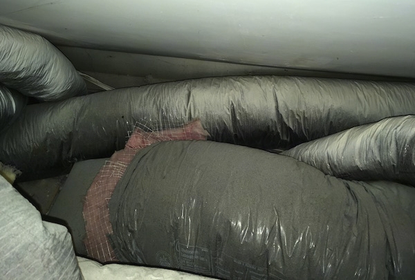 Large, dusty black flex ducts with exposed pink fiberglass insluation showing.