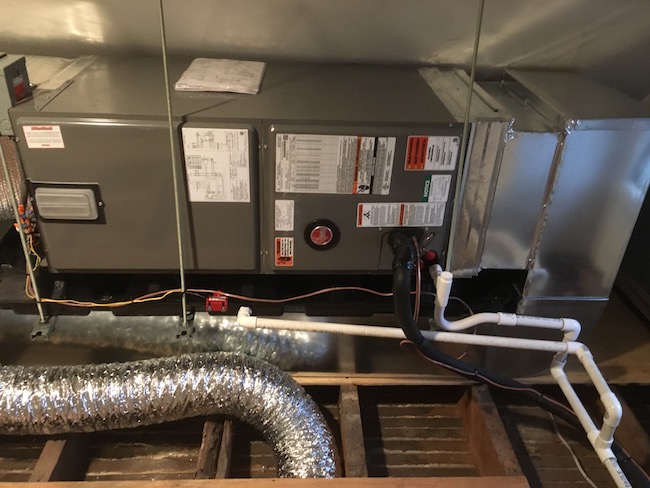 A heat pump air handler with foil flex ducts coming from it running under the floor in an attic