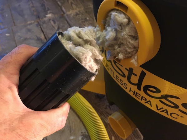 A person holding the end of a shop vac tube that was removed from the vac. There is gray fiberglass all clogged up in the tube and in the unit.