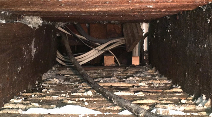 A view inside of a wooden floor cavity showing wires running through it.