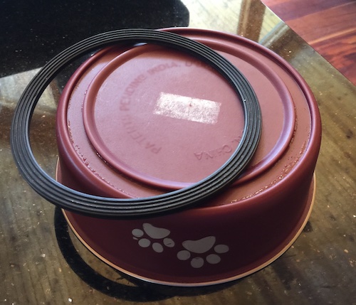 An upside-down maroon dog bowl with white paw prints on it with the rubber bottom pried off