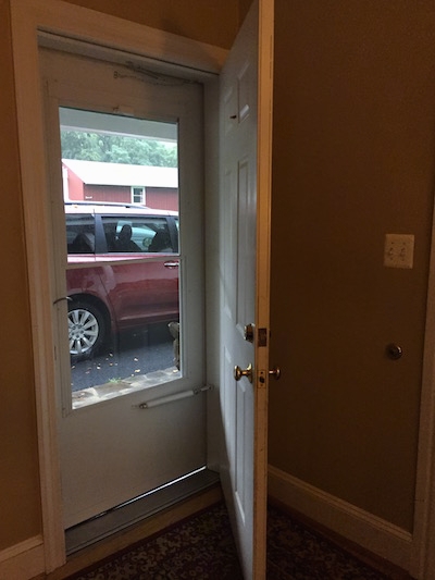 An open door with a closed storm door leading to the outside in a house.