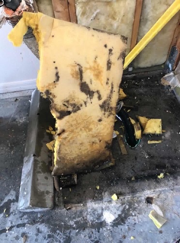 A moldy sheet of yellow fiberglass leaning against more yellow fiberglass inside of a dirty HVAC unit.