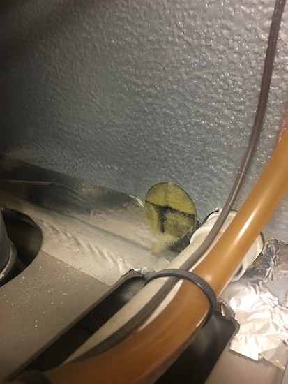 Yellow fiberglass coming out of a round hole that was cut at the bottom of a heater next to pipes and wires.