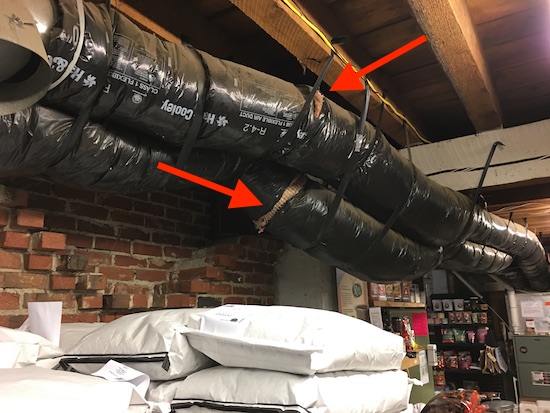 A feed store with black flex ductwork running above the ceiling that has exposed fiberglass. There are bags of feed and things for sale on shelves in the distance.
