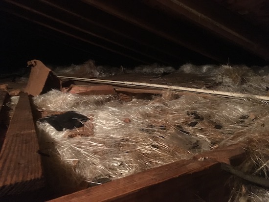 An attic floor filled with loose white strands of thin glass fibers