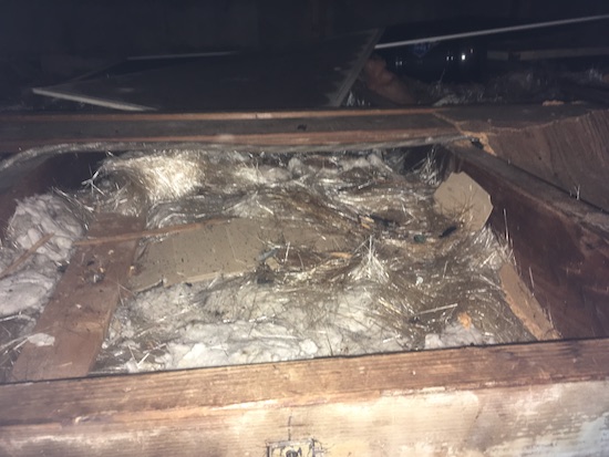White strands of glass fibers laying on top of blown in fiberglass in an attic of a home