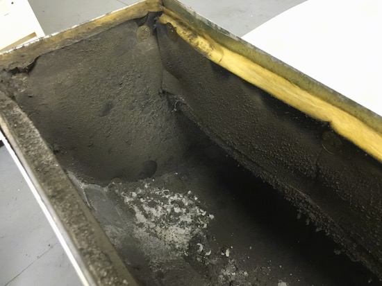 A section of a fiberglass lined duct with lots of black dirt all over the inside and yellow insulation