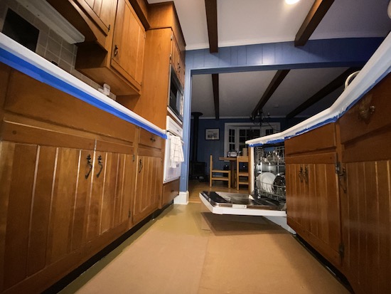 A blue kitchen with an open dishwasher and blue painters tape all around the bottom of the countertop overhang.