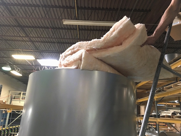 A gloveless bare hand installing fiberglass insulation into a round metal tube.