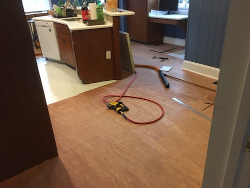 Brown plywood on top of a linoleum floor in a blue kitchen with tools on the floor