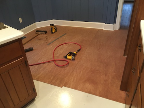 Brown plywood on top of a linoleum floor in a blue kitchen