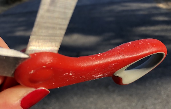 A person with a red painted fingernail holding a pair of scissors with strands of glass stuck all over it from static electricity.