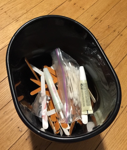 A black plastic trash can with a bunch of emry boards and other manicure supplies