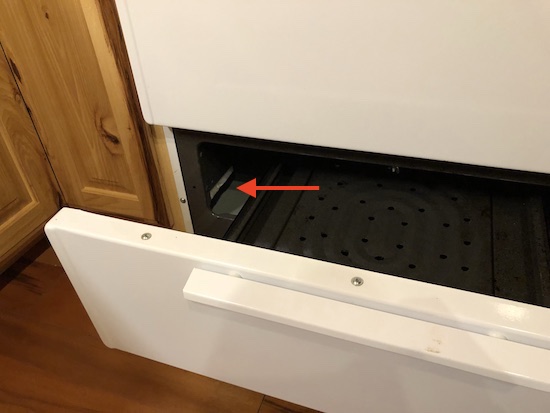 A white oven with the broiler door open and a red arrow pointing to white ceramic fiber wool that is exposed inside of it.