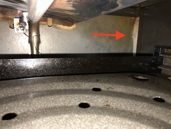 A view of the back of a gas oven just past the broiler pan is an arrow pointing to the right side at exposed white ceramic fiber wool.