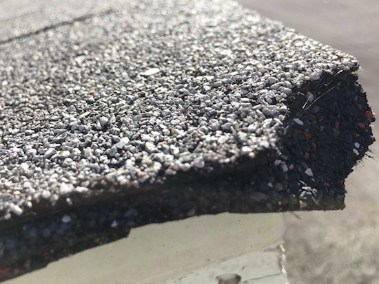 The corner of a roof shingle with the end missing. You can see tiny hair-like fibers poking out.