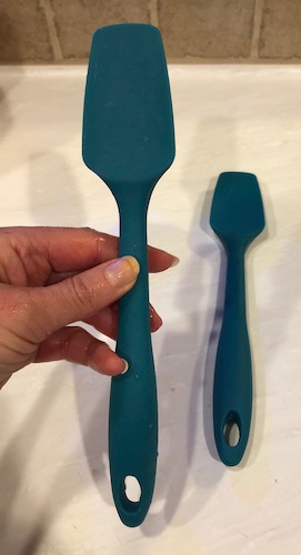 A teal blue-green rubber cake scraper being held by a person