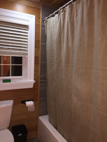 A tan hemp shower curtain hanging over a white metal tub in a bathroom