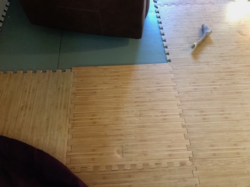A brown foam mat on a gray floor with a dog bone laying on the mat