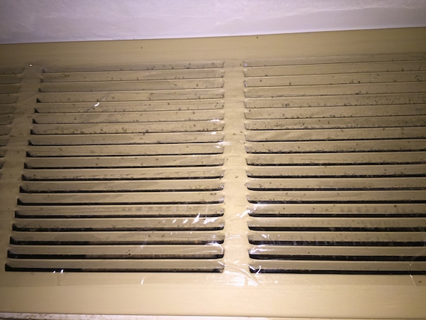 A beige ceiling vent taped over with clear packing tape with gray fiberglass dust sticking to the sticky side.