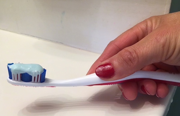 Toothpaste on a toothbrush being held by a lady with red fingernails