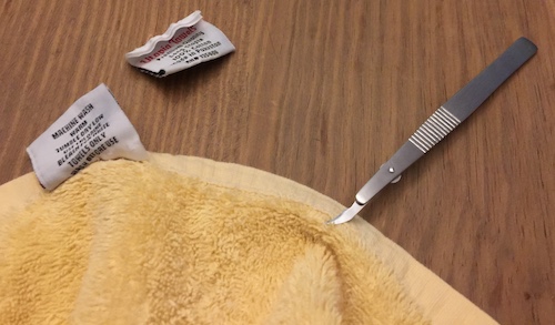 A yellow cotton towel with rayon tags on it and a seam stripper tool that I used to remove the tags
