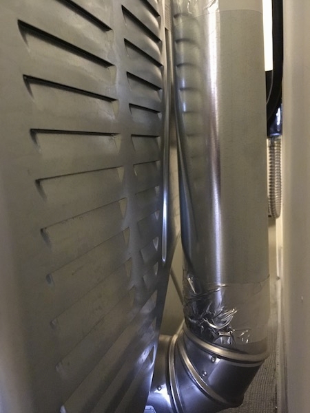 The back of a vented dryer showing the vents that suck air into the dryer and a silver tube that runs up the wall to vent the air outside.