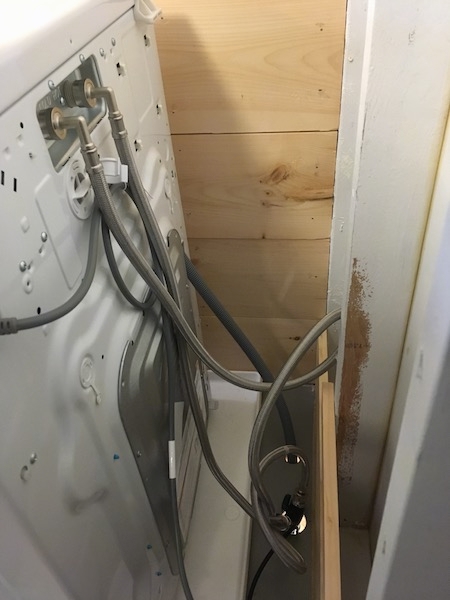 The backside of a ventless washer dryer combo showing water tubes, a drain tube and a power cord.