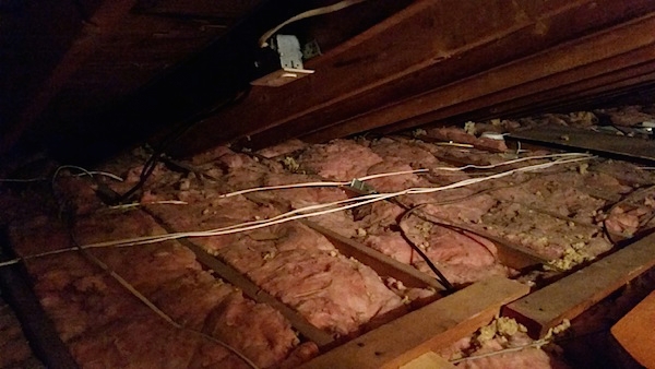 Pink fiberglass batts in-between the rafters up in an attic of a house with wires an an outlet.