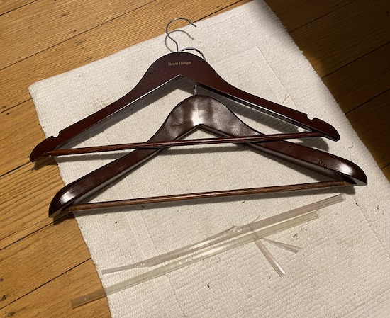 Two wooden hangers on a white mat on a hardwood floor with the plastic shrink wrap that was removed laying below them